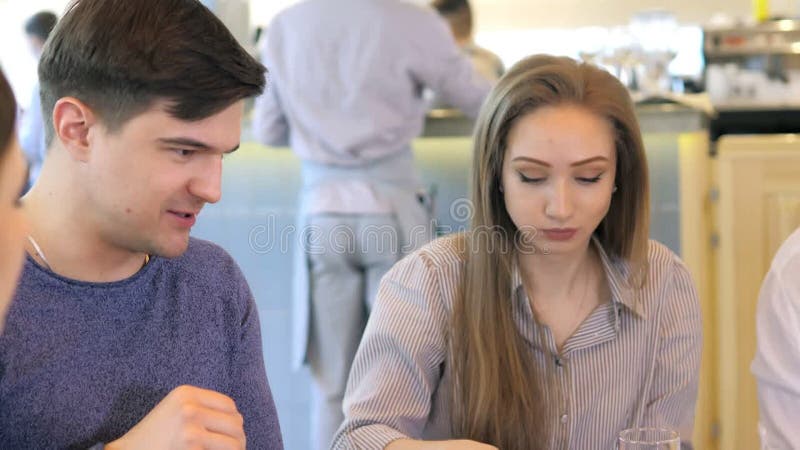 Un groupe d'amis heureux s'installe à table dans un restaurant cosy riant et s'amusant. un groupe de filles et d'hommes clips vidéos