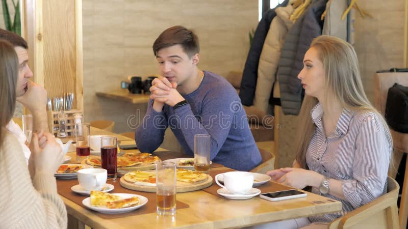 Un groupe d'amis heureux s'installe à table dans un restaurant cosy riant et s'amusant. un groupe de filles et d'hommes banque de vidéos