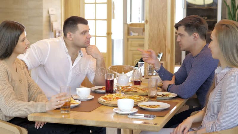 Un groupe d'amis heureux s'installe à table dans un restaurant cosy riant et s'amusant. un groupe de filles et d'hommes clips vidéos
