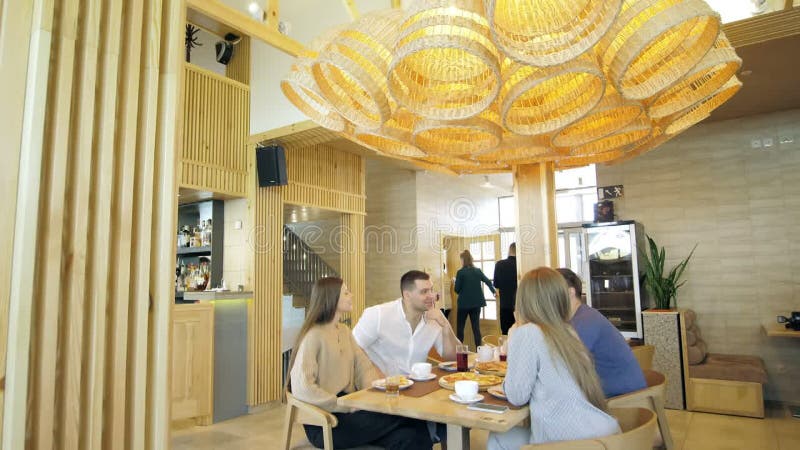 Un groupe d'amis heureux s'installe à table dans un restaurant cosy riant et s'amusant. un groupe de filles et d'hommes banque de vidéos