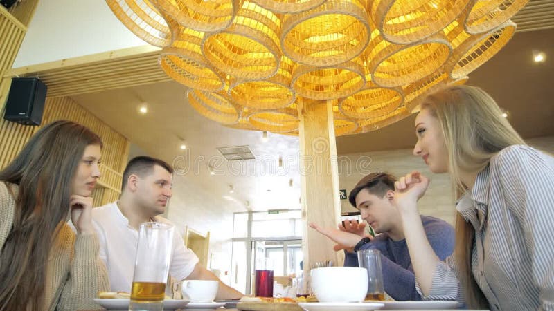 Un groupe d'amis heureux s'installe à table dans un restaurant cosy riant et s'amusant. un groupe de filles et d'hommes banque de vidéos