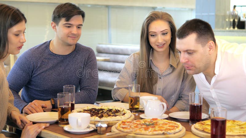 Un groupe d'amis heureux s'installe à table dans un restaurant cosy riant et s'amusant. un groupe de filles et d'hommes banque de vidéos
