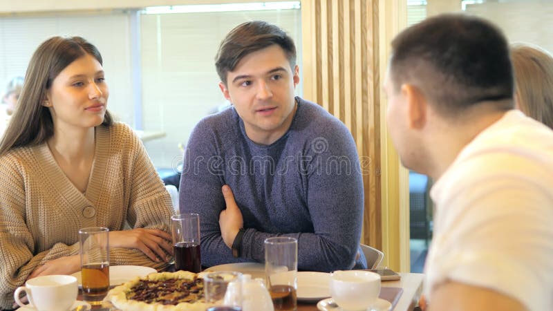 Un groupe d'amis heureux s'installe à table dans un restaurant cosy riant et s'amusant. un groupe de filles et d'hommes clips vidéos
