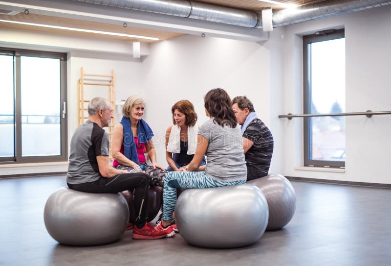 Un groupe d'aînés dans le gymnase se reposant après avoir fait l'exercice sur les boules convenables, parlant photos libres de droits Un groupe d'aînés dans le gymnase se reposant après avoir fait l'exercice sur les boules convenables, parlant photos libres de droits