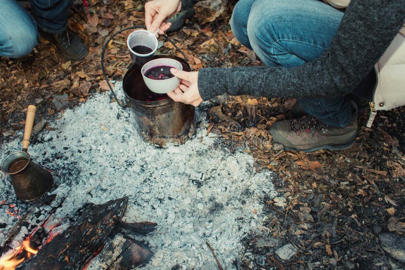 A group of people drinking tea, coffee and mulled wine in the outdoor. Mulled wine, tea and coffee cooked over a campfire on the nature. A group of people drinking tea, coffee and mulled wine in the outdoor. Mulled wine, tea and coffee cooked over a campfire on the nature.