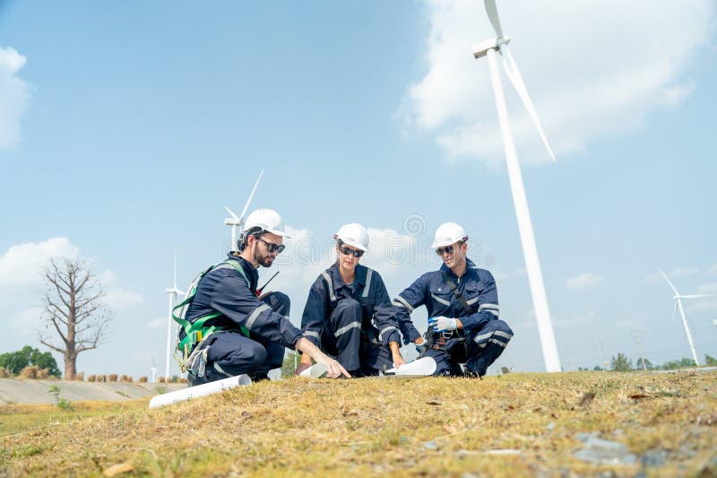 Un groupe de techniciens professionnels discutent du travail avec le plan du projet sur papier devant l'éolienne ou l'éolienne et photographie stock libre de droits