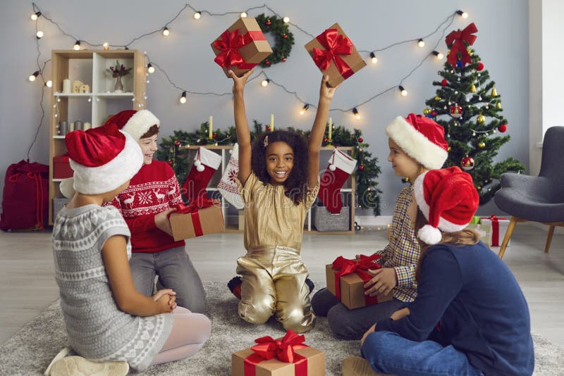 Un gruppo di bambini felici e multietnici che si scambiano regali seduti sul pavimento in salotto immagini stock