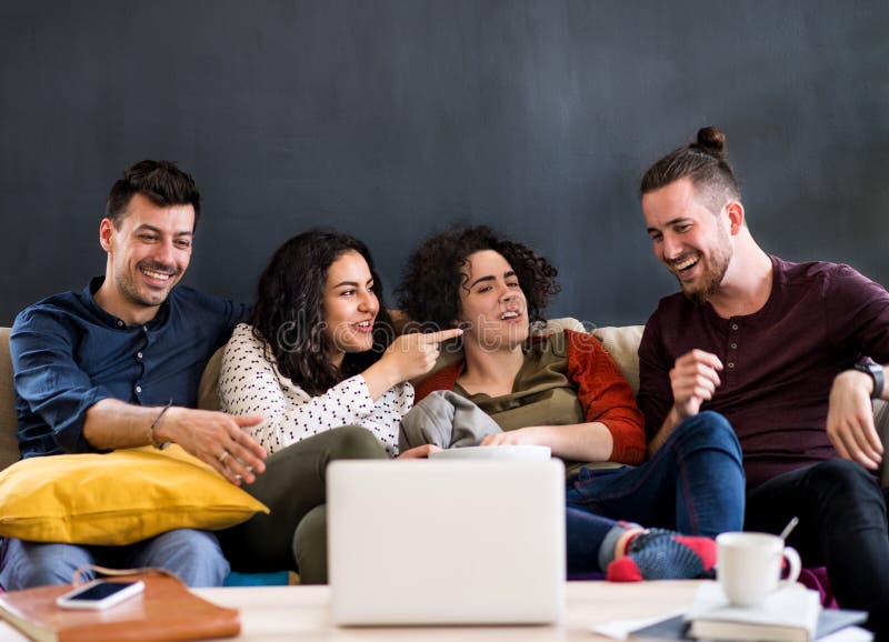 Un gruppo di giovani amici con un computer portatile seduto sul divano al chiuso a guardare il film immagine stock libera da diritti Un gruppo di giovani amici con un computer portatile seduto sul divano al chiuso a guardare il film immagine stock libera da diritti