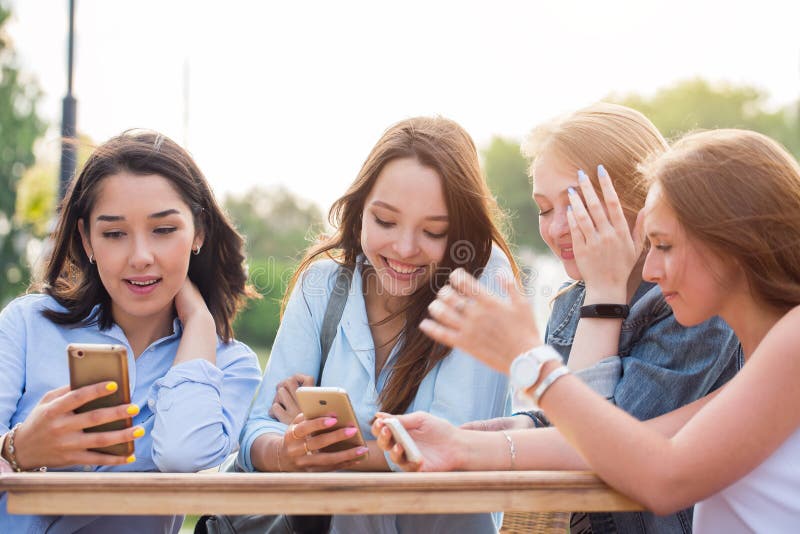 Un gruppo di studenti delle ragazze che si siedono ad una tavola nel parco e con un sorriso che discute qualcosa smartphones dell fotografie stock libere da diritti Un gruppo di studenti delle ragazze che si siedono ad una tavola nel parco e con un sorriso che discute qualcosa smartphones dell fotografie stock libere da diritti