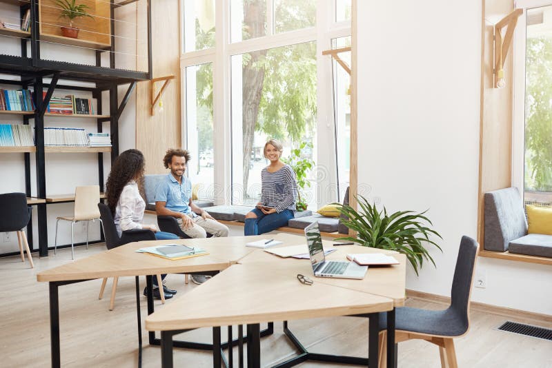 Un gruppo di tre giovani multi partenze etniche che lavorano insieme nello spazio coworking, avendo rottura da 'brainstorming' gi immagini stock libere da diritti Un gruppo di tre giovani multi partenze etniche che lavorano insieme nello spazio coworking, avendo rottura da 'brainstorming' gi immagini stock libere da diritti