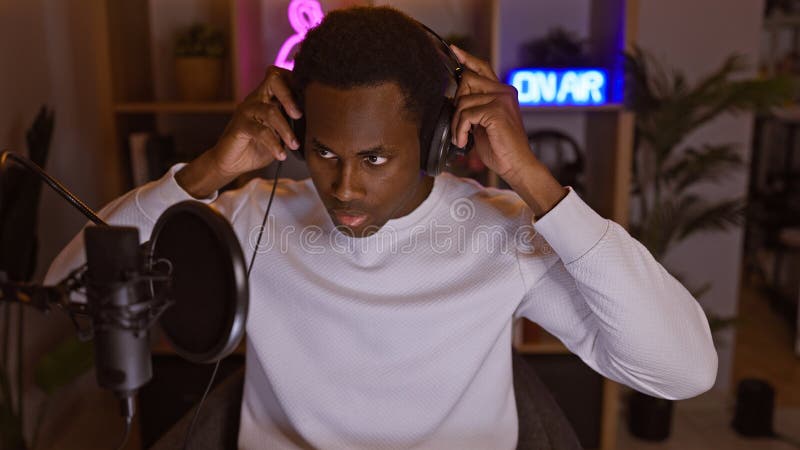 Un hombre adulto enfocado en los auriculares en una sala de juegos para casa iluminada con micrófono y aire acondicionado fotos de archivo