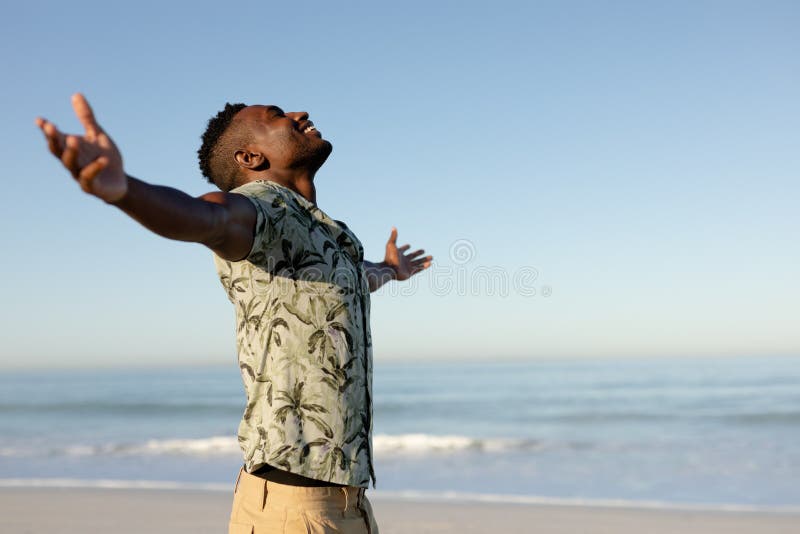 Un hombre afroamericano con los brazos extendidos en la playa en un día soleado