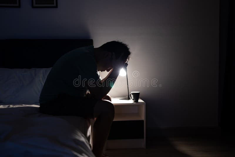 Un hombre asiático deprimido llorando cubriendo la cara con las manos sentadas en la cama por la noche preocupados por la gente qu