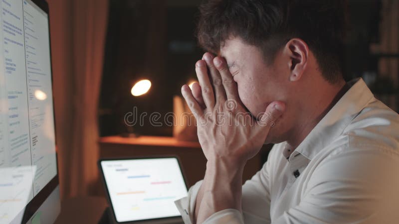 Un hombre asiático trabaja solo en una computadora de escritorio en su oficina, cansado y estresado por el trabajo Horas extraord