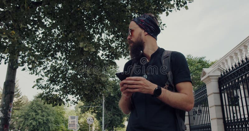 Un hombre barbudo camina por las calles urbanas enfocado en su celular almacen de video