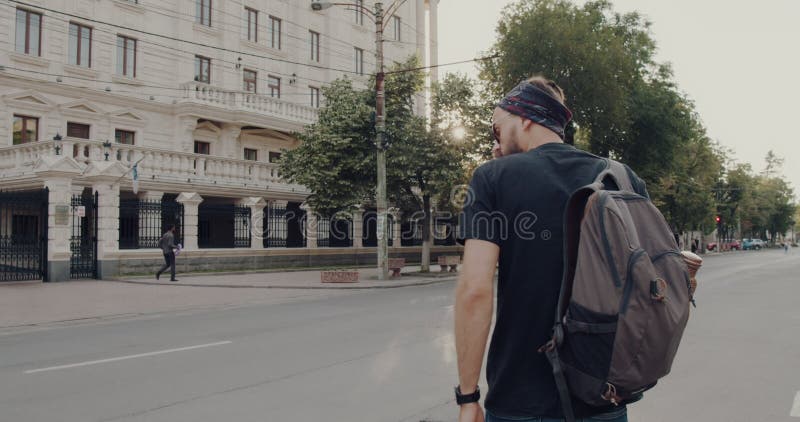 Un hombre barbudo con gafas de sol se pasea por una ciudad con una mochila metrajes