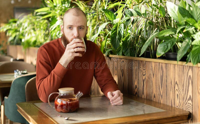 Un hombre barbudo muy guapo disfrutando de un té caliente. Hombre caucásico bebe té de fruta en una cafetería verde. foto de archivo libre de regalías