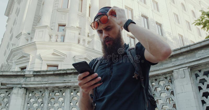 Un hombre barbudo navega por la ciudad mientras interactúa con su teléfono metrajes