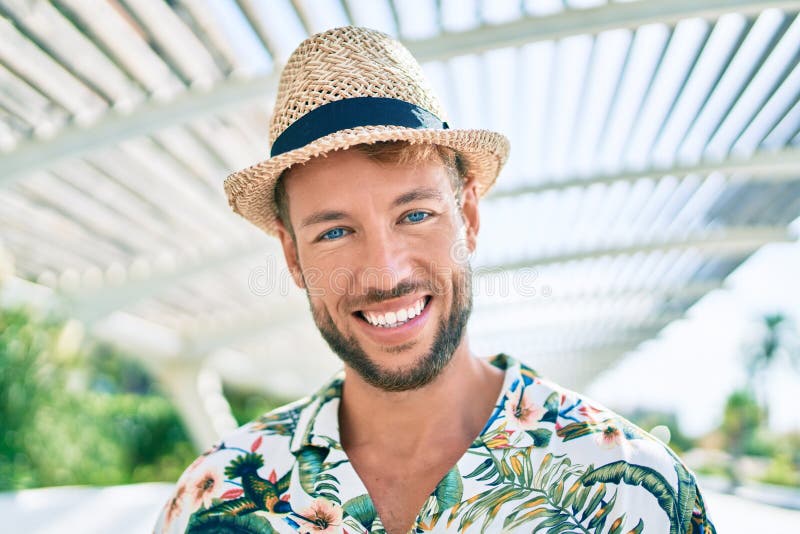 Un hombre caucásico guapo que lleva sombrero de verano y camisa floral sonriendo feliz al aire libre fotografía de archivo libre de regalías