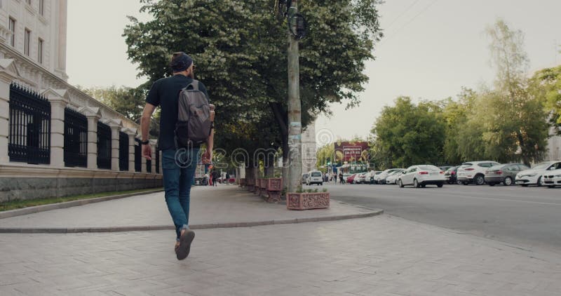 Un hombre con mochila camina por una vibrante calle de la ciudad abrazando la aventura almacen de video