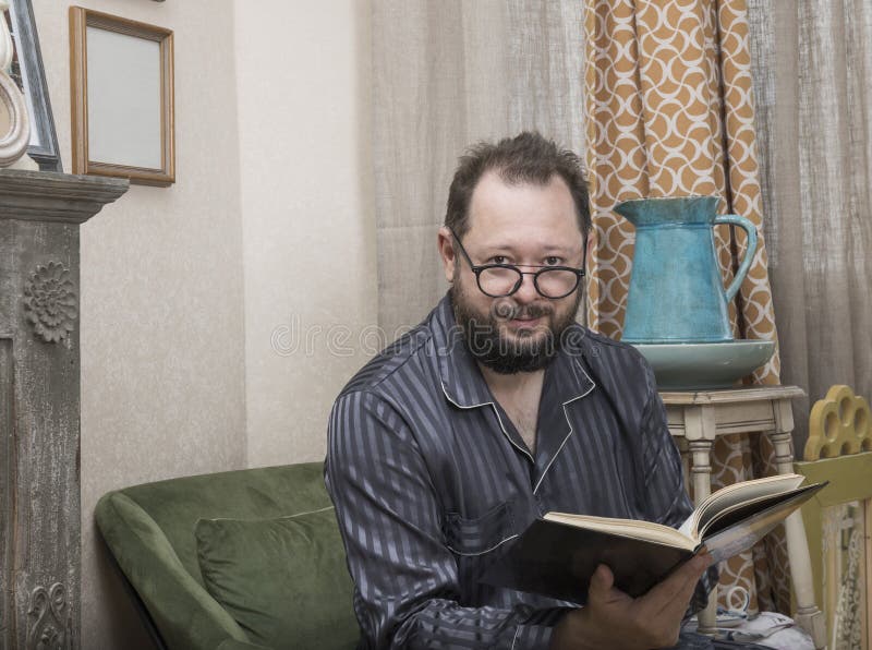 Un hombre con una barba en sus pijamas lee un libro fotografía de archivo Un hombre con una barba en sus pijamas lee un libro fotografía de archivo