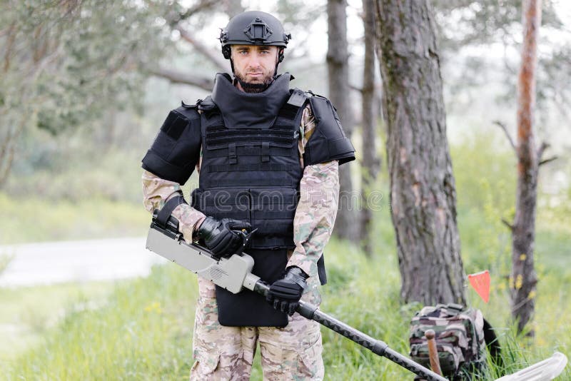 Un hombre con uniforme militar y chaleco antibalas trabaja en el bosque  para desminar el territorio