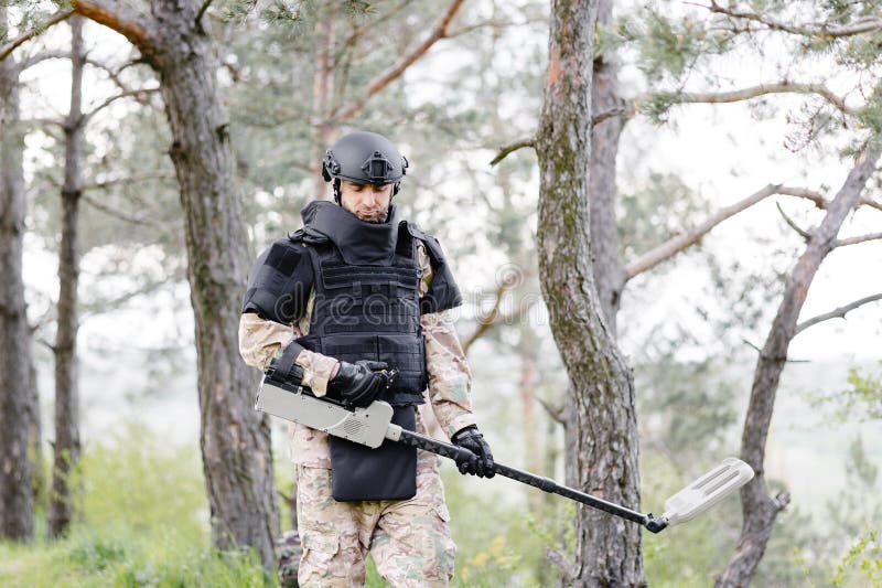 Un Hombre Con Uniforme Militar Y Un Chaleco Antibalas Trabaja En El Bosque  Para Desminar El Territorio. Un Hombre Se Pone Un Casco Imagen de archivo -  Imagen de armado, profundamente: 277401063