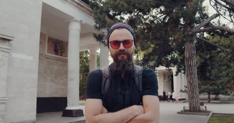 Un hombre de confianza, con barba y gafas de sol, se encuentra junto a un edificio moderno metrajes