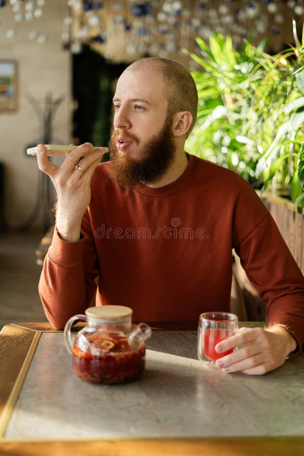 Un hombre de milenio guapo que usa el reconocimiento de voz del teléfono sentado en una acogedora cafetería fotos de archivo libres de regalías