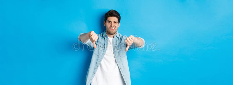 Un hombre decepcionado que muestra su pulgar hacia abajo y se queja de algo horrible que no le gusta a un producto que juzga una m fotografía de archivo