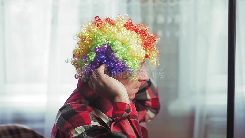 Un hombre delante de un espejo pone una peluca de payaso con rizos multicolores