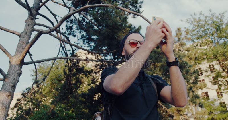 Un hombre disfruta de la naturaleza tomando selfies y fotos de un árbol majestuoso almacen de metraje de vídeo