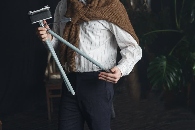 un hombre en una camisa blanca y un suéter marrón está sosteniendo un trípode viejo con una cámara, un vintage fotografía de archivo un hombre en una camisa blanca y un suéter marrón está sosteniendo un trípode viejo con una cámara, un vintage fotografía de archivo