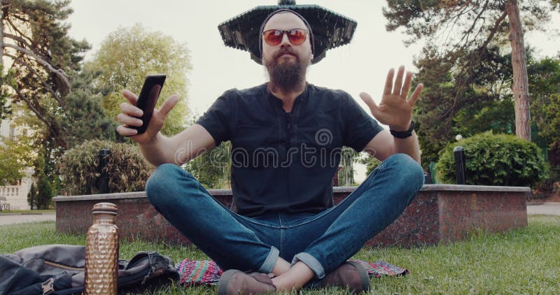 Un hombre en una pose de loto usa su teléfono en un parque tranquilo almacen de metraje de vídeo