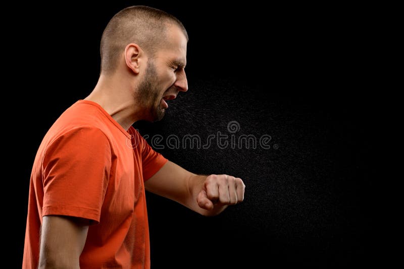 A sneezing man with drops of saliva on a black isolated background. The concept of the spread of diseases by airborne droplets Studio photo. A sneezing man with drops of saliva on a black isolated background. The concept of the spread of diseases by airborne droplets Studio photo