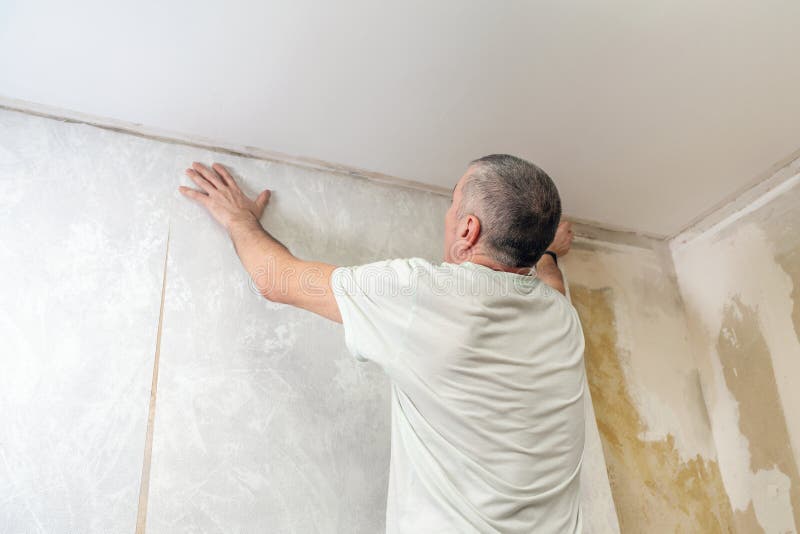 A man is gluing non-woven wallpaper on the wall. Room renovation. A man is gluing non-woven wallpaper on the wall. Room renovation.