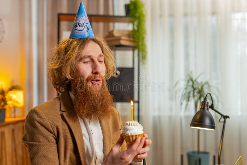 Un hombre feliz de oficina de negocios usa una fiesta de cumpleaños que contiene bizcochito hace que el deseo sople una vela ardie fotos de archivo
