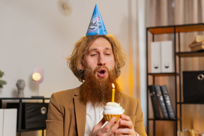 Un hombre feliz de oficina de negocios usa una fiesta de cumpleaños que contiene bizcochito hace que el deseo sople una vela ardie foto de archivo libre de regalías