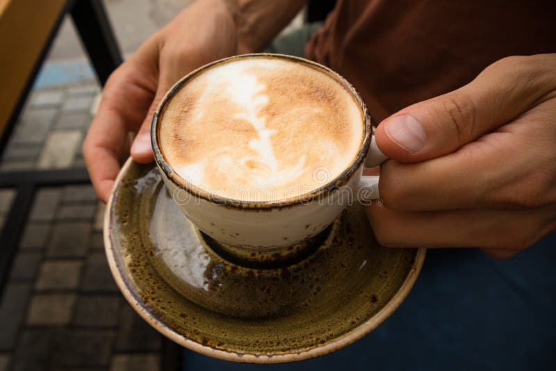 Un hombre hermoso joven se está sentando en un café con los amigos y el capuchino caliente de consumición, relajación, cercana pa foto de archivo libre de regalías Un hombre hermoso joven se está sentando en un café con los amigos y el capuchino caliente de consumición, relajación, cercana pa foto de archivo libre de regalías