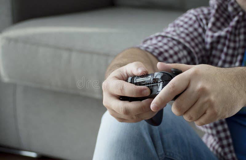 Un hombre joven con la palanca de mando que juega a los videojuegos en casa que pasa t imagen de archivo Un hombre joven con la palanca de mando que juega a los videojuegos en casa que pasa t imagen de archivo