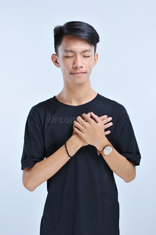 Un hombre joven está tocando su corazón para la solidaridad humanitaria con los ojos cerrados y gesto agradecido en cara Concepto