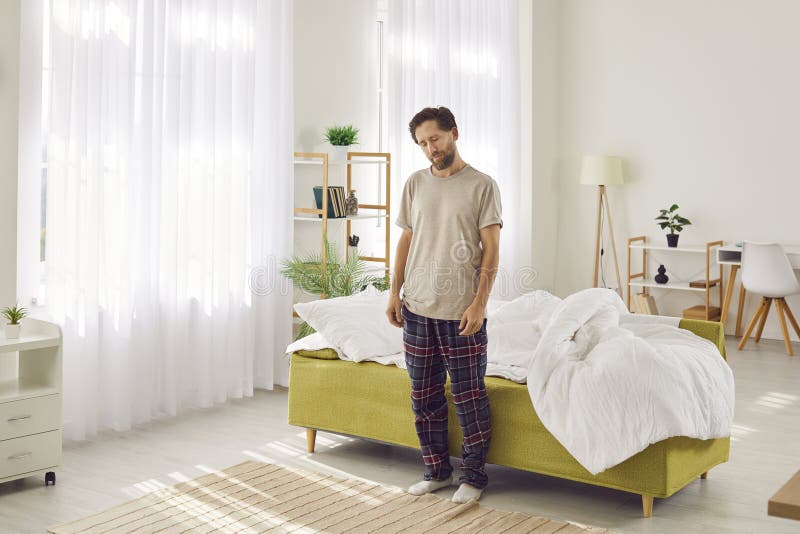 Un hombre joven y dormido que padece de sonambulismo parado con los ojos cerrados cerca de su cama en casa. fotos de archivo libres de regalías