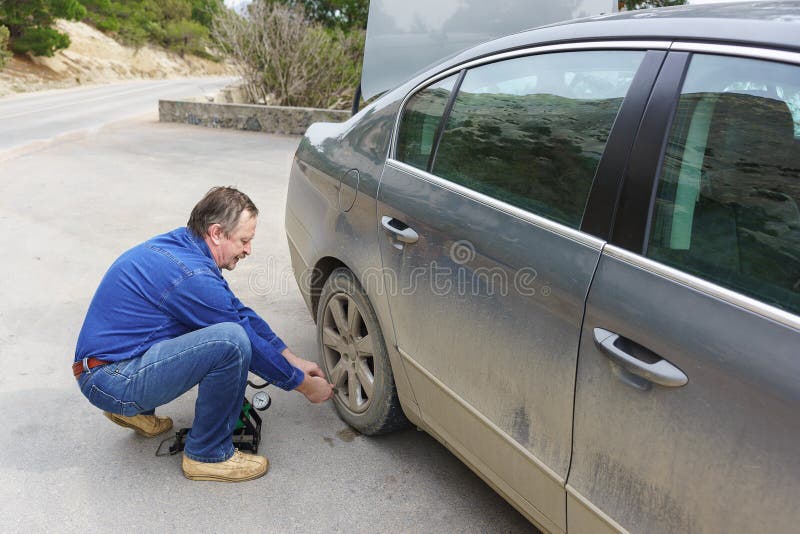 Un hombre mayor bombea la rueda de un coche sucio imágenes de archivo libres de regalías Un hombre mayor bombea la rueda de un coche sucio imágenes de archivo libres de regalías