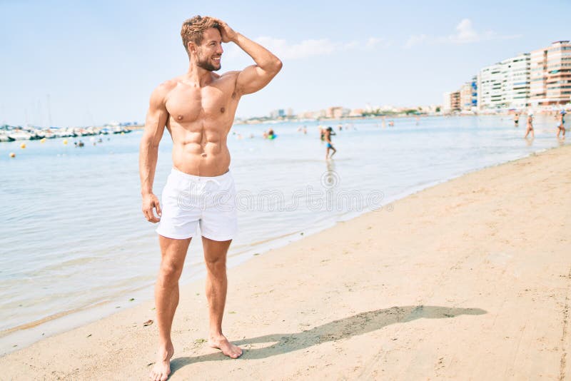 Un hombre muy bonito y caucásico de fitness en la playa en un día soleado mostrando el cuerpo muscular de la salud fotos de archivo
