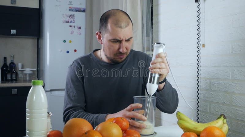 Un hombre preparando un cóctel fresco con un mezclador de frutas en una batidora de la cocina. un hombre prepara un almacen de metraje de vídeo