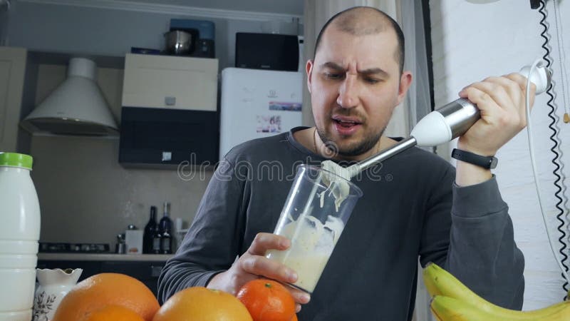 Un hombre preparando un cóctel fresco con una batidora de frutas en una licuadora de la cocina. un hombre prepara un sano y nutrit almacen de video