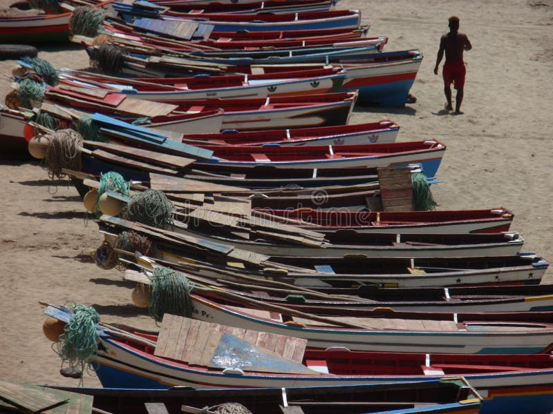 Un hombre que camina en la playa de Tarrafal al lado de muchos pequeños barcos de madera coloridos fotografía de archivo libre de regalías Un hombre que camina en la playa de Tarrafal al lado de muchos pequeños barcos de madera coloridos fotografía de archivo libre de regalías