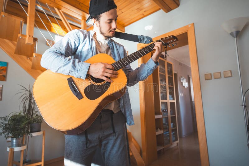 Un hombre solo en medio de una sala iluminada por el sol disfruta tocando una hermosa guitarra acústica de madera y componiendo nu imagen de archivo libre de regalías