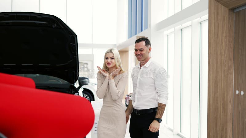 Un hombre sorprende a una mujer rubia con un auto nuevo con el arco rojo en la sala de exposición metrajes
