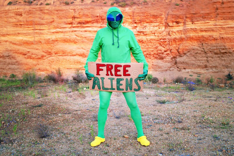 Un Hombre Vestido Con Traje De Carnaval Extraterrestre Verde En Una Sola Manifestación Con Un Cartel Un Hombre Vestido Con Traje De Carnaval Extraterrestre Verde En Una Sola Manifestación Con Un Cartel